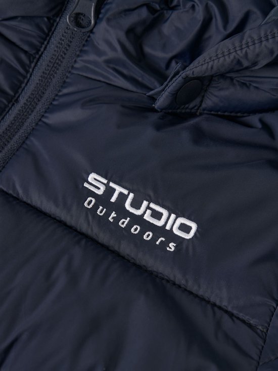 Detail van de donkerblauwe gewatteerde jas met opdruk 'STUDIO OUTDOORS'.