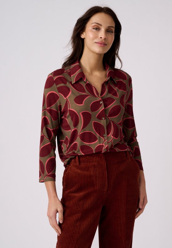 Mannequin portant une blouse verte à imprimé graphique bordeaux et un pantalon en velours côtelé marron.