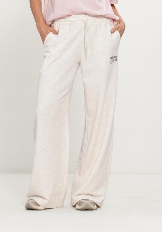 Lichtbeige wijde New Balance broek met geborduurd logo op de linkerheup, gedragen door een model.