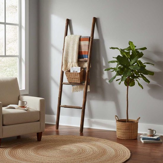Donkerbruine decoratieve ladder met een gebreide handdoek en een mandje, in een woonkamer.