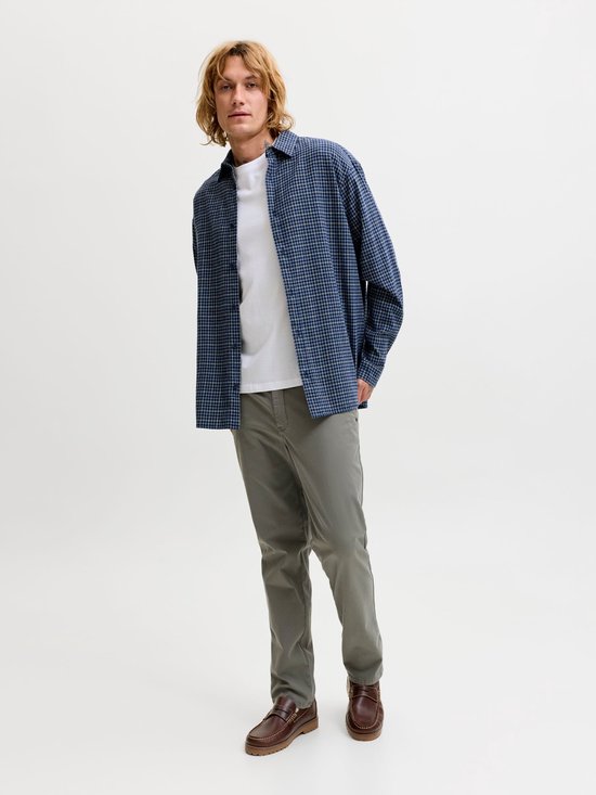 Man met blonde haren, draagt grijze chino, wit T-shirt en blauw geruit overhemd.