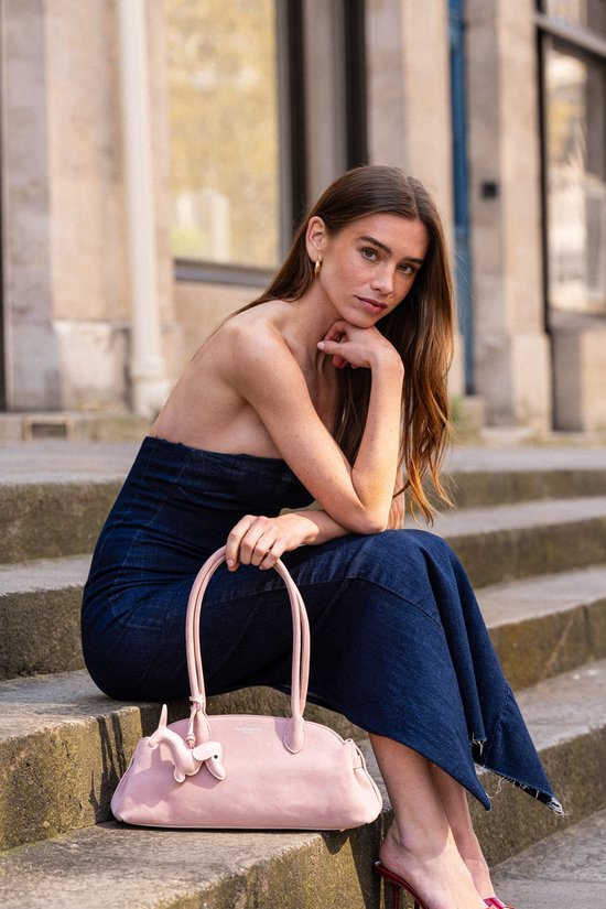 Model met een lichtroze handtas met teckel versiering, zittend op een trap.