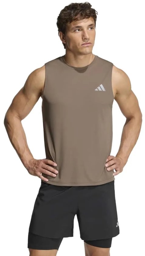 Man in bruin mouwloos sportshirt met logo en zwarte shorts, handen in de zij.