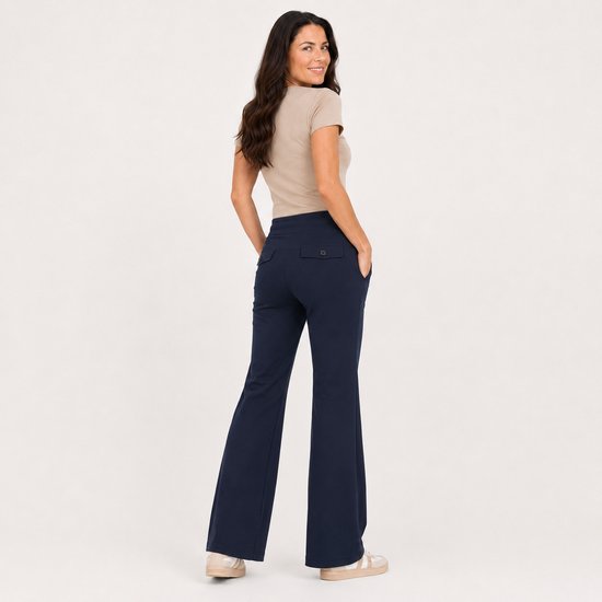 Vrouw in een beige top en marineblauwe flared broek met twee achterzakken, van achteren gezien, kijkend over haar schouder.