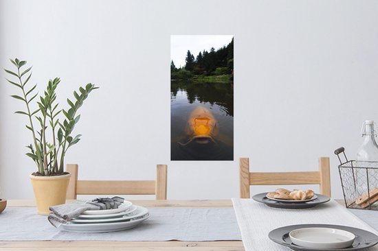 Une grande carpe koï orange nage dans un étang avec des arbres en arrière-plan.