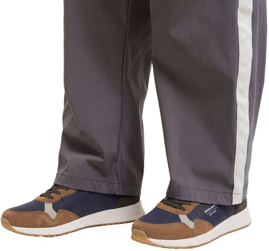 Donkerblauwe en bruine Jack & Jones sneakers met witte zolen, gedragen met een grijze broek met witte streep.