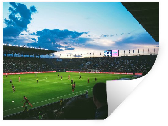 Stade de football au coucher du soleil avec le public dans les gradins et les joueurs sur le terrain.