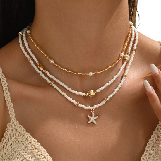 Een model draagt drie gouden kettingen: een met parel, een met schelp en een met witte zeester hanger.