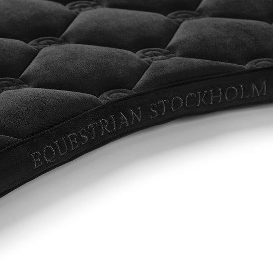Close-up van de rand van een zwart zadeldek met de tekst 'Equestrian Stockholm' in reliëf.
