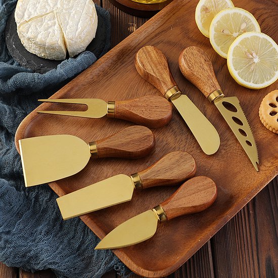 Gouden kaasmesjes met houten handvatten liggen op een houten plank naast een stuk kaas en citroenschijfjes.