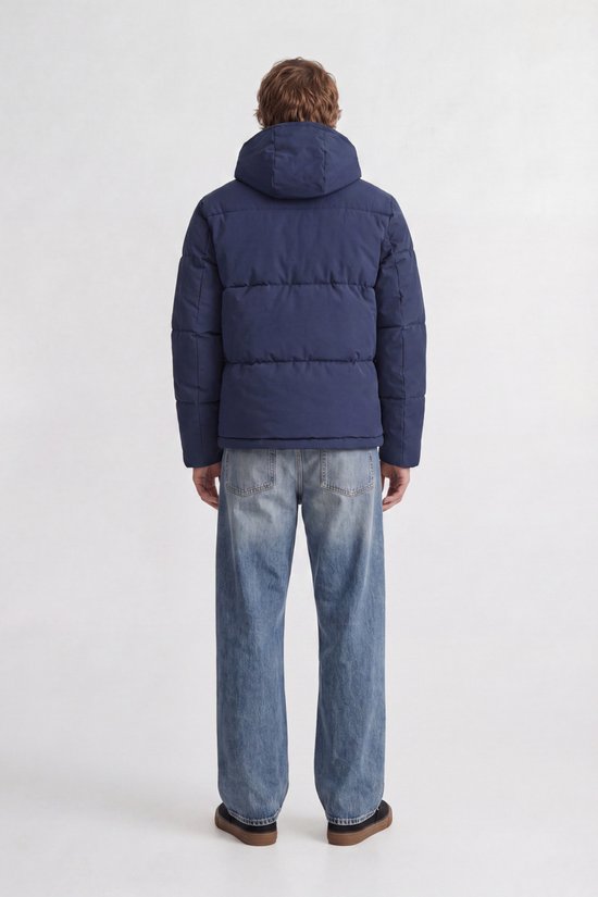 Achterkant man met donkerblauwe pufferjas met capuchon, witte t-shirt en wijde spijkerbroek.