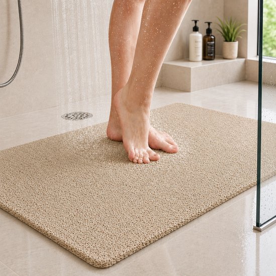 Beige douchemat met antislip textuur waarop iemand met blote voeten staat onder de douche.