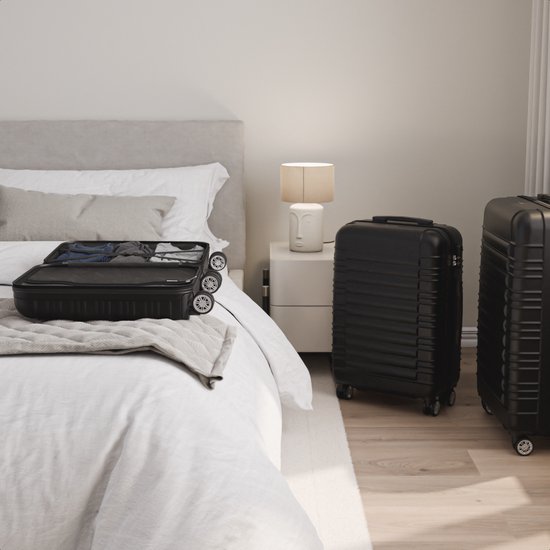 Een open zwarte TRVLMORE koffer gevuld met kleding op een bed, met een gesloten koffer ernaast.
