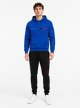 Man in een blauwe hoodie met 'PARIS' tekst en rode/zwarte streepjes, en een zwarte joggingbroek met 'PARIS' tekst.