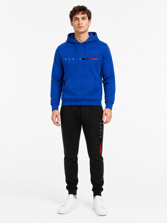 Man in een blauwe hoodie met 'PARIS' tekst en rode/zwarte streepjes, en een zwarte joggingbroek met 'PARIS' tekst.