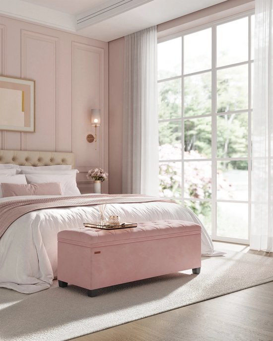 Roze gestoffeerde opbergkruk met deksel staat op een slaapkamer bij een bed.