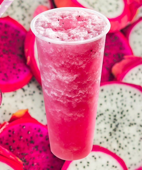 Roze drakenvruchten smoothie met schuim, omringd door gesneden drakenvruchten.