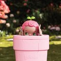 Luvibubs pop kijkt vanuit een roze pot. Het heeft roze, krullend haar met twee groene blaadjes.
