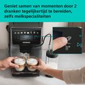 Twee handen houden glazen latte macchiato onder Siemens volautomaat espressomachine. Melkreservoir ernaast.