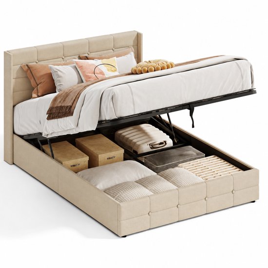 Beige gestoffeerd bed met opklapbare lattenbodem, vol met opbergdozen, koffers en kussens.
