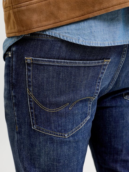 Close-up van de achterzak van een donkerblauwe spijkerbroek met gele stiksels.