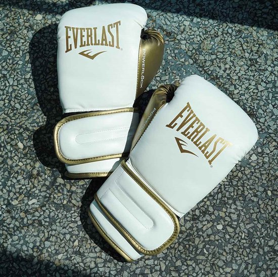 Twee witte Everlast bokshandschoenen met gouden accenten, liggend op een stenen ondergrond.