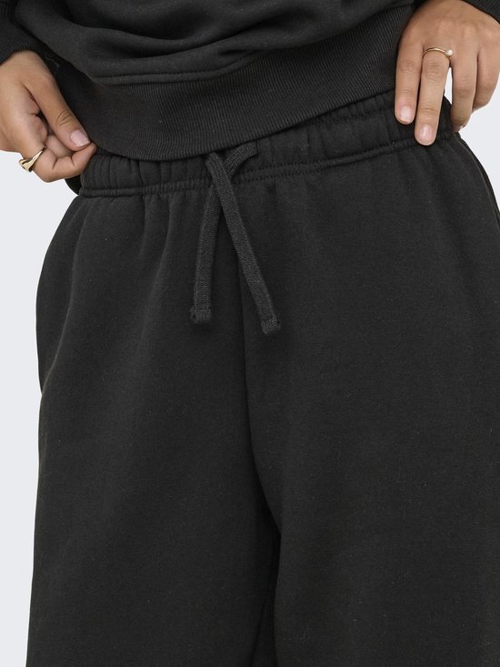 Close-up van de tailleband van een zwarte joggingbroek met trekkoord en zakken. Een model trekt aan de stof.