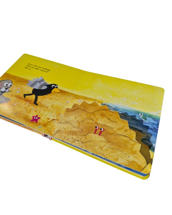 Gottmer flappenboek 'Coco op het strand' open op een pagina met zandduinen, de zee en Coco de kraai. Een zeehond kijkt over de rand van een duin.
