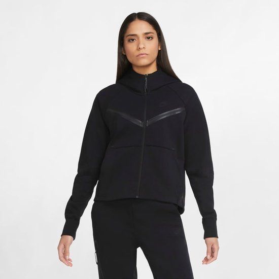 Vrouw draagt een zwarte Nike Tech Fleece hoodie met rits en Nike-logo op de borst.