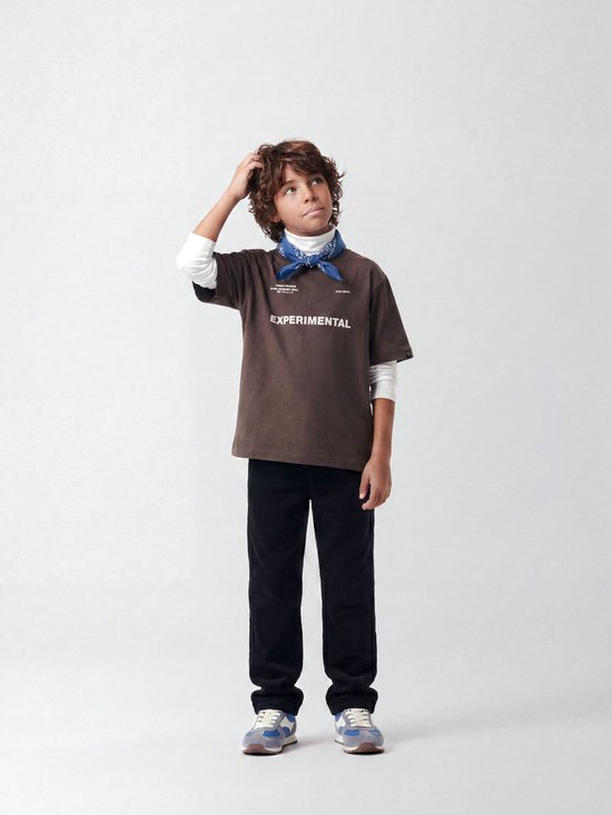 Jongen in bruin t-shirt met tekst 'EXPERIMENTAL', wit shirt eronder en blauwe bandana.