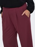 Close-up van een bordeauxrode broek met wijde pijpen, plooien en steekzakken.
