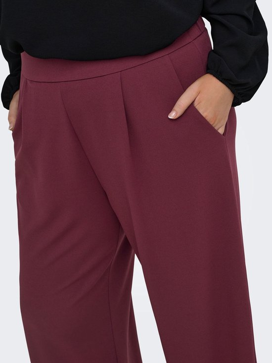 Close-up van een bordeauxrode broek met wijde pijpen, plooien en steekzakken.
