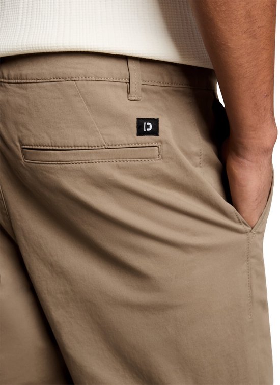 Sluiting van de achterzak van een beige chino met een zwart label.