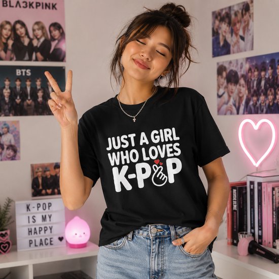 Een vrouw met een zwarte t-shirt met de tekst "JUST A GIRL WHO LOVES K-POP" en een vingerhartje, maakt een V-teken.