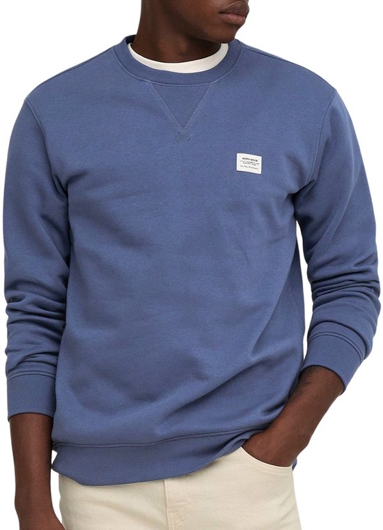 Close-up van man in blauwe sweater met V-stiksel en een label met 'WORKWEAR' op de borst.