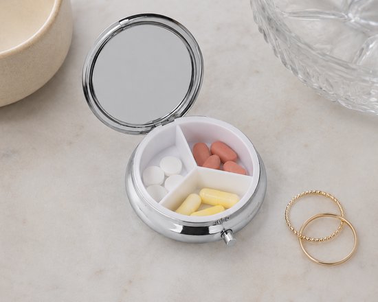 Zilverkleurig pillendoosje open, met 3 vakjes gevuld met witte, gele en roze pillen. Inclusief spiegel.