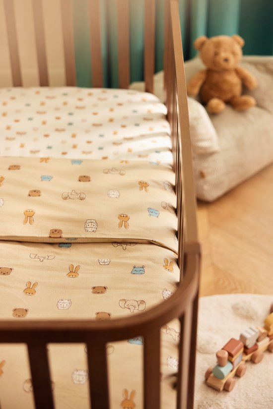 Een ledikant met een beige hoeslaken met een print van beige en blauwe dierenkoppen. Bovenop ligt een wit hoeslaken met dezelfde print.