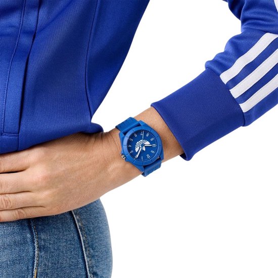 Persoon met blauw Adidas horloge om de pols, gedragen met een blauw trainingsjack met witte strepen.
