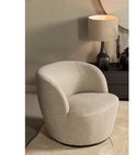 Een lichte fauteuil met een ronde, draaiende vorm, gestoffeerd in een zandkleurige geweven stof, met een lamp en decoratie op de achtergrond.