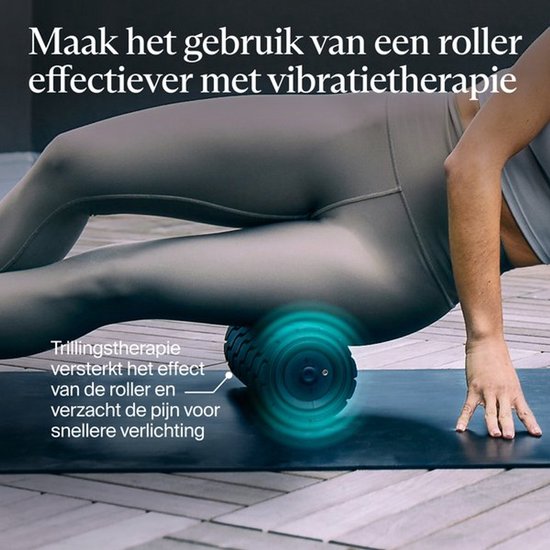 Een vrouw gebruikt een schuimroller met vibratietherapie op haar been op een yogamat.