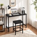 Zwart bureau met laptop, lamp en mok koffie, naast een kruk en boekenplank.