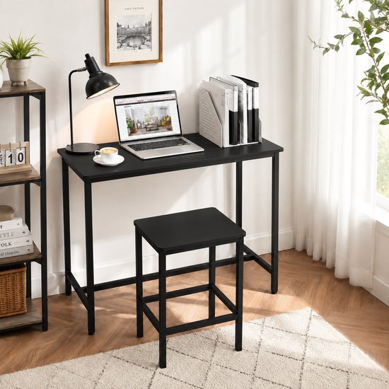 Zwart bureau met laptop, lamp en mok koffie, naast een kruk en boekenplank.