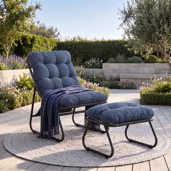 Fauteuil de salon bleu foncé en velours côtelé avec pouf, avec une couverture en laine sur le fauteuil, dans un jardin.