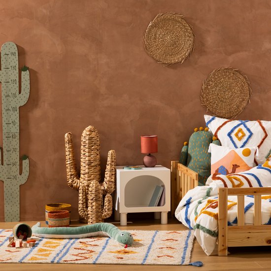 Kinderkamer met houten bed, beddengoed met geometrische patronen, decoratieve cactus van waterhyacint, een slangenkussen en een cactus-wanddecoratie.
