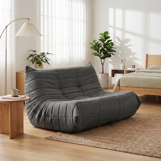 Grijze, zachte vloersofa met gewatteerde rug en zitvlak, in een lichte woonkamer.