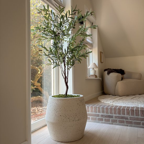 Een kunstmatige olijfboom met groene bladeren en zwarte olijven staat in een grote, ruwe, gebroken witte bloempot.