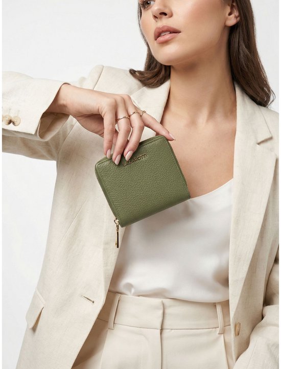 Vrouw met beige blazer, witte top en gouden ringen, laat olijfgroene portemonnee zien.