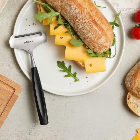 Boska kaasschaaf met zwart handvat op een bord met een belegd broodje.