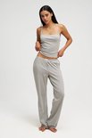 Model in een grijze pyjama met spaghettibandjes top en wijde broek, staand op witte achtergrond.