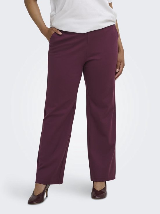 Model met lange bordeauxrode broek met rechte pijpen, witte top en hakken.